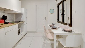 A compact kitchen with white cabinets, a wooden countertop, and a dining area with a white table and chairs. - Bluestay 301 - Superb apartment in Paris (Paris 02 Bourse)