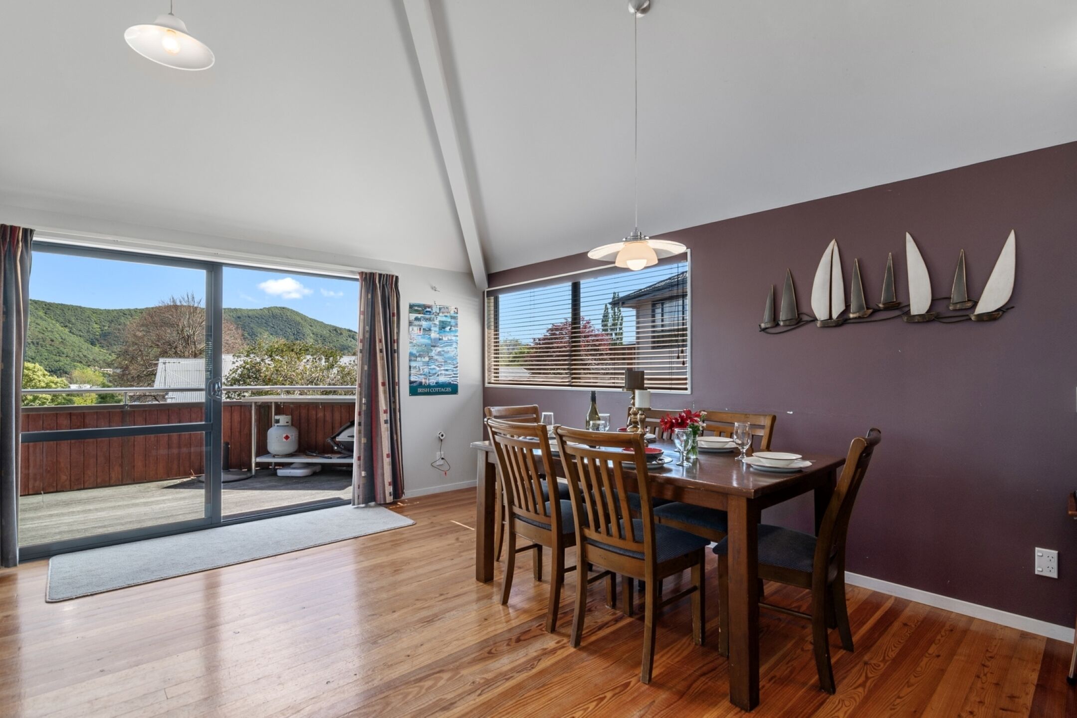 A dining area with a wooden table and chairs, a view of the outdoors through large sliding glass doors, and a purple wall with decorative elements.