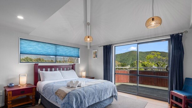 Een moderne slaapkamer met een groot bed, een nachtkastje, een bijzettafeltje, een raam met uitzicht op groen en een balkon met houten hekwerk.