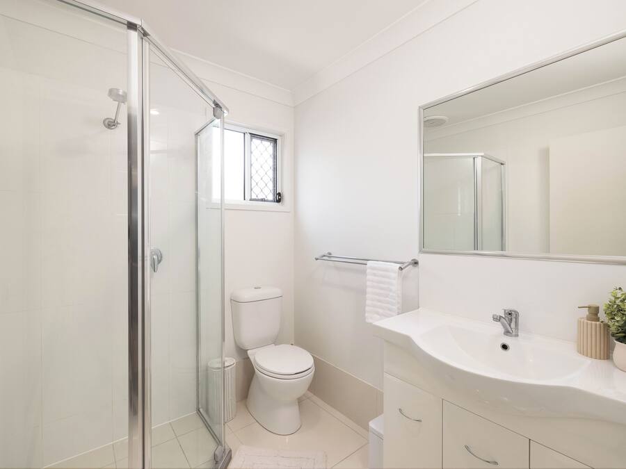 A modern bathroom with a glass shower enclosure, a toilet, and a sink with a mirror above it.