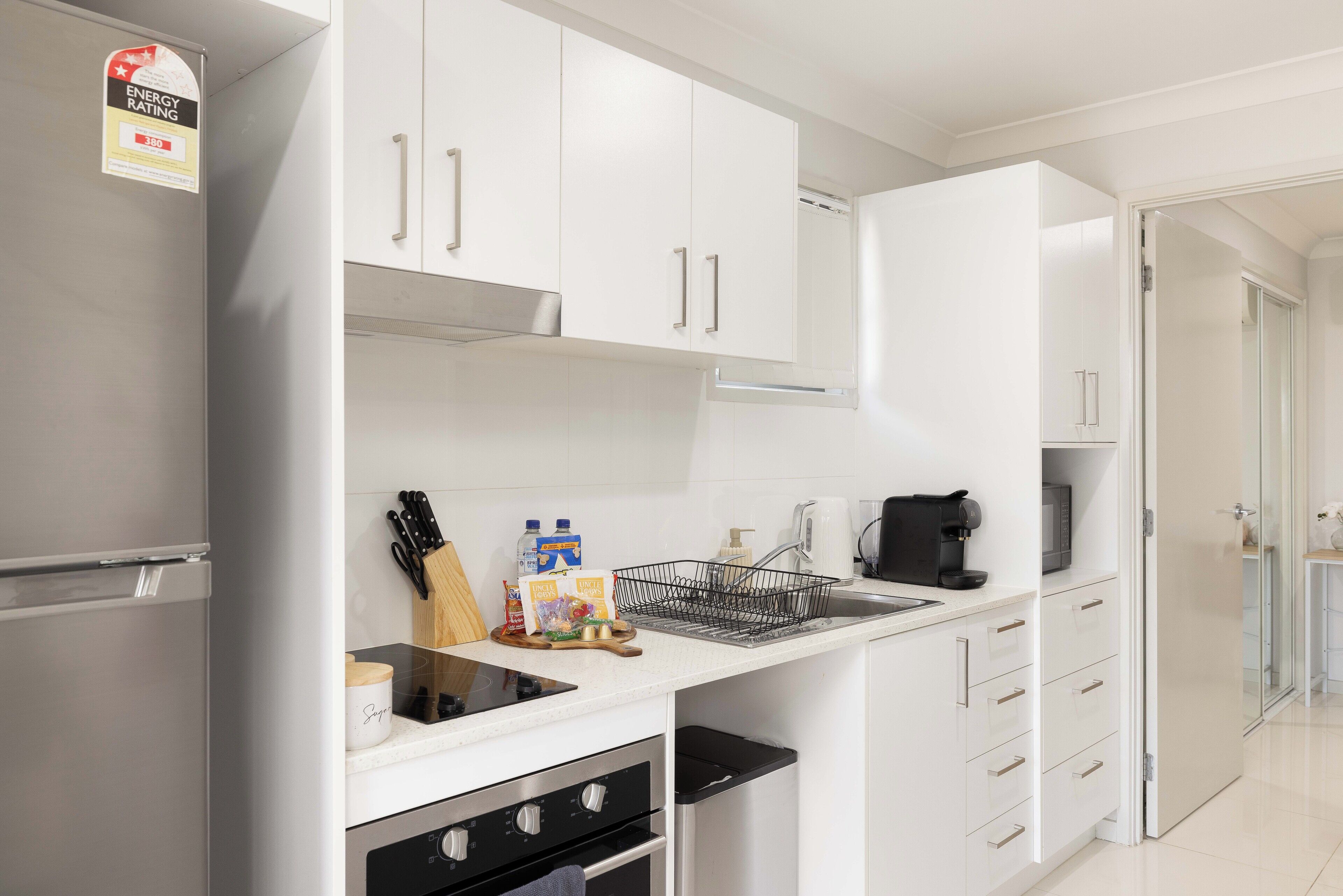 Une cuisine moderne avec des meubles blancs, des appareils en acier inoxydable et une machine à café.