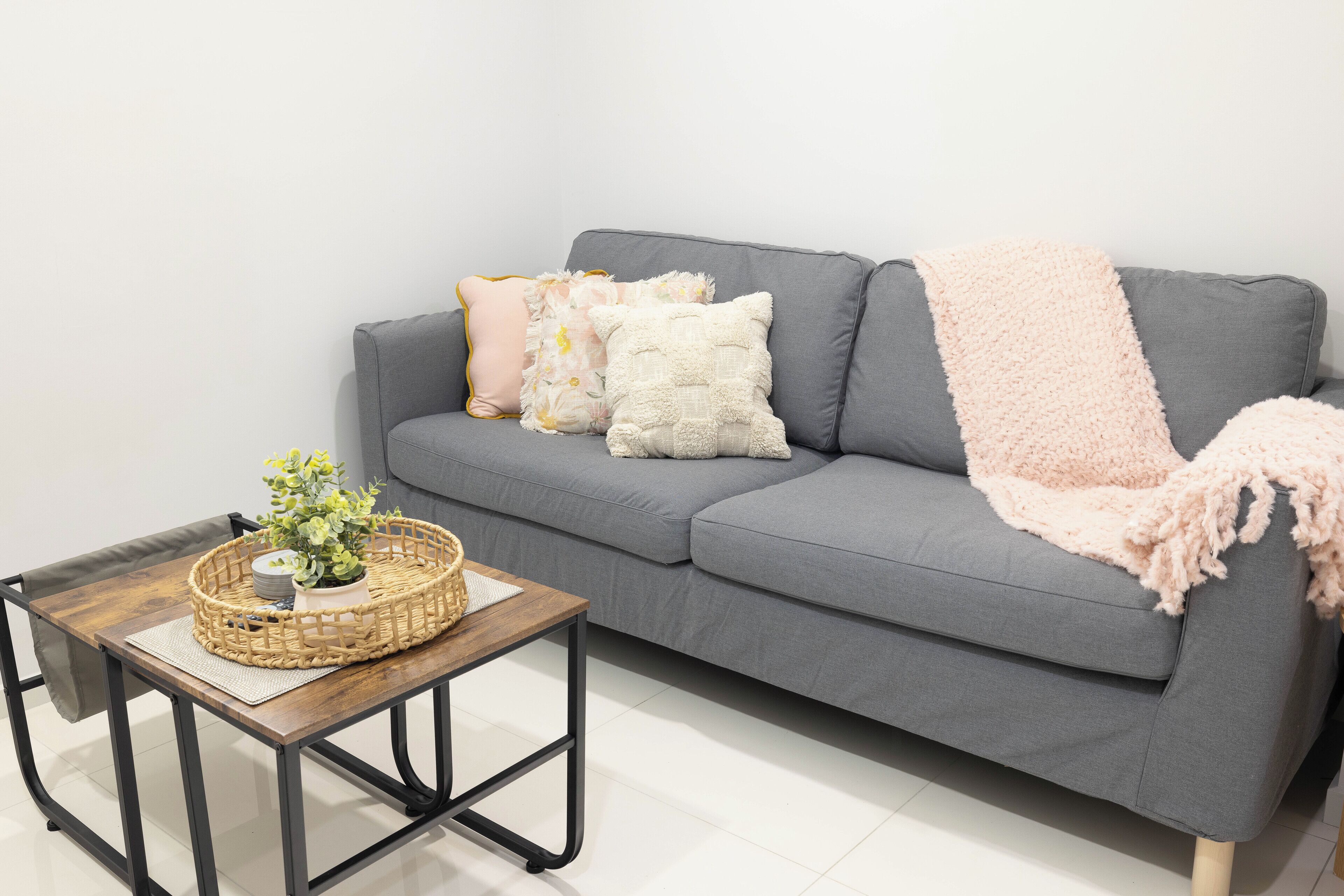 A grey sofa with a pink throw blanket, a wooden coffee table with a woven basket, and decorative pillows.