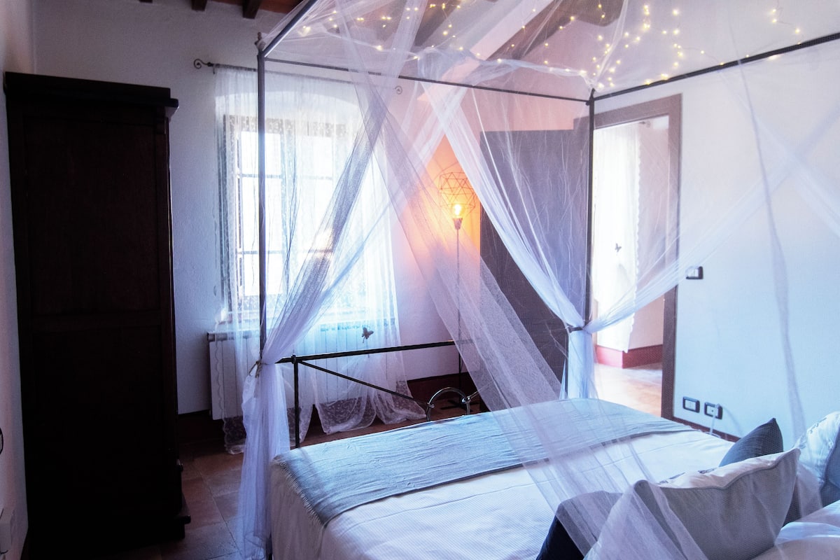 A bedroom with a four-poster bed, a canopy, and a view of the outdoors.
