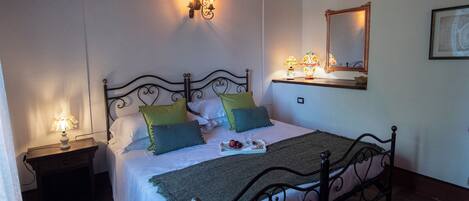 A neatly made bed with a green throw blanket, a bedside table with a lamp, and a wall-mounted mirror.