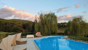 A swimming pool with lounge chairs and a tent, surrounded by trees and hills.