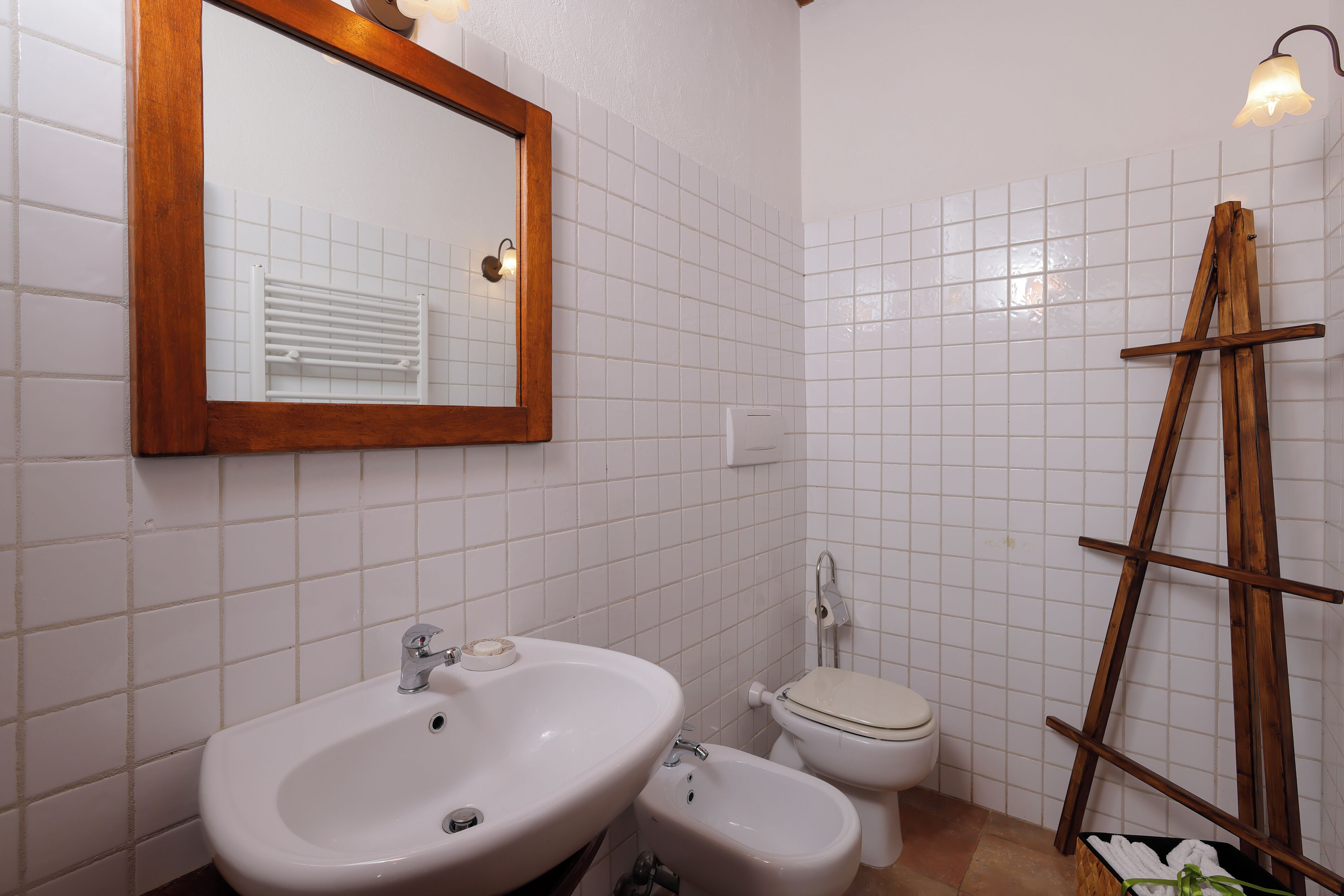 Une salle de bain avec un miroir encadré en bois, un lavabo, un bidet et une échelle en bois appuyée contre le mur.