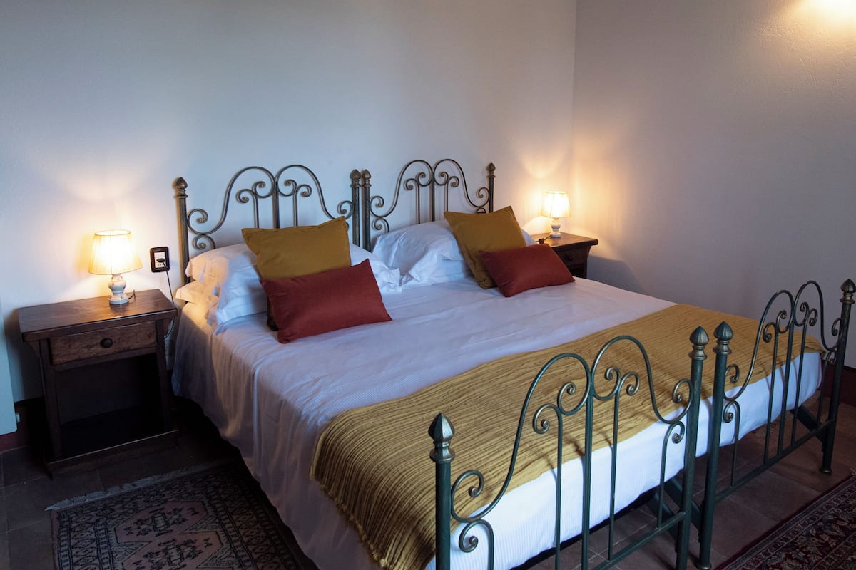 A neatly made bed with a metal frame, two bedside tables with lamps, and a patterned rug on the floor.