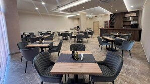 Un restaurant moderne doté de nombreuses tables et chaises, d’un bar et d’une cuisine située à l’arrière.