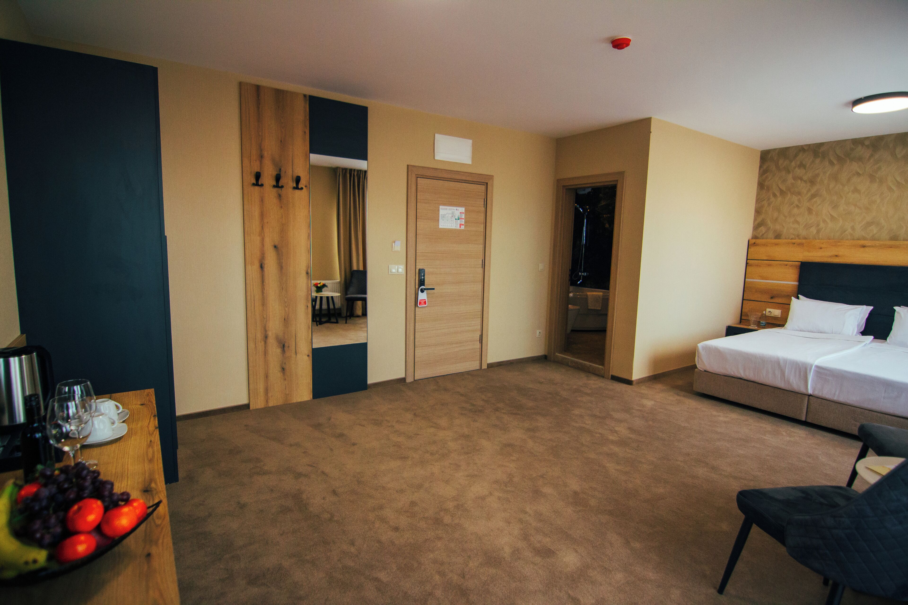 A hotel room with a bed, a desk with a fruit bowl, a chair, and a door leading to a bathroom.