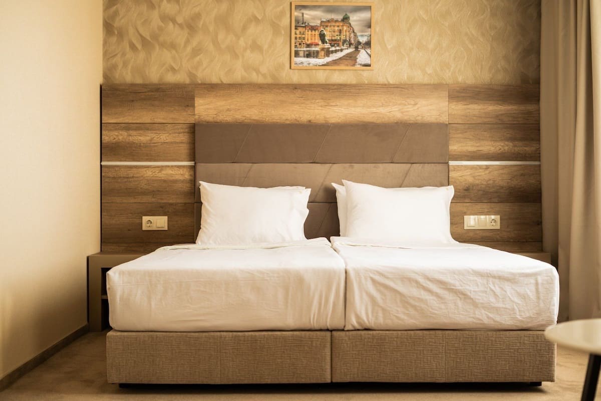 A double bed with a wooden headboard and two pillows, a nightstand, and a framed picture on the wall.