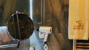 A bathroom with a marble wall, a sink, a mirror, a towel rack, and a hairdryer.