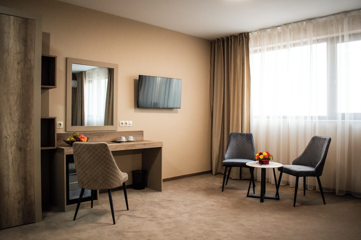 A hotel room with a desk, two chairs, a television, and a large window with curtains.