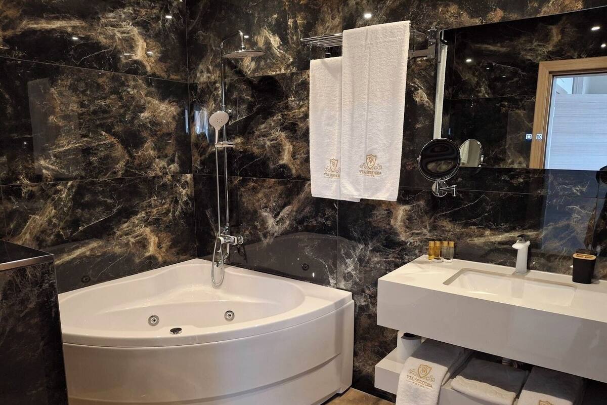 A modern bathroom with a freestanding bathtub, a vanity with a mirror, and marble walls.