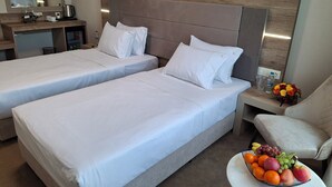 Une chambre d’hôtel avec deux lits, un petit bureau avec une machine à café, une chaise et un panier de fruits.