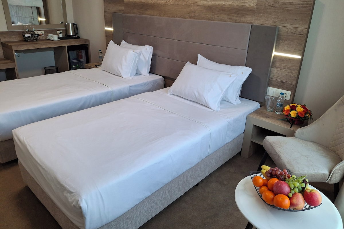 A hotel room with two beds, a small desk with a coffee maker, a chair, and a fruit basket.