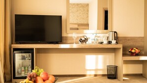 Une chambre d’hôtel équipée d’une télévision, d’un minibar, d’un panier de fruits et d’une petite poubelle.