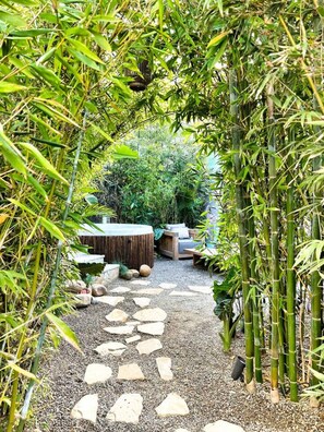 A garden pathway with stepping stones, bamboo plants, and a seating area with a round table and chairs.