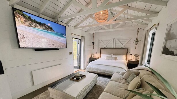A bedroom with a large bed, a smaller bed, a sofa, a TV, and a ceiling fan.