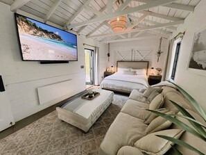 A bedroom with a large bed, a smaller bed, a sofa, a TV, and a ceiling fan.