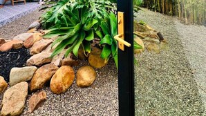 A modern house with a glass door leading to a garden with rocks, plants, and a view of bamboo trees.