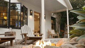 A patio area with a fire pit surrounded by rocks, wooden chairs, and a view of the house.
