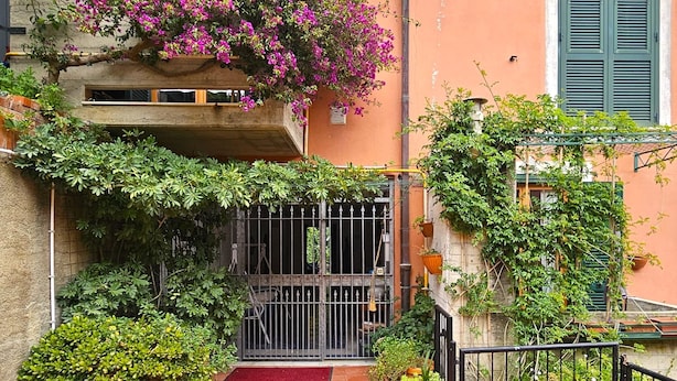 A narrow alleyway with a gated entrance, surrounded by lush greenery and flowering plants.