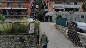 A narrow cobblestone street flanked by multi-story buildings with balconies and a stone wall with a metal gate.
