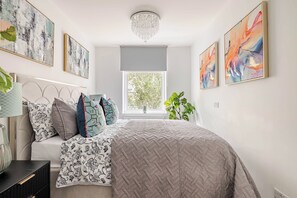 A bedroom with a bed, a nightstand, a lamp, a window, and wall art.