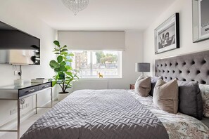 Ein Schlafzimmer mit einem großen Bett, einem Fernseher, einer Pflanze und einem Fenster mit Blick auf die Stadt.