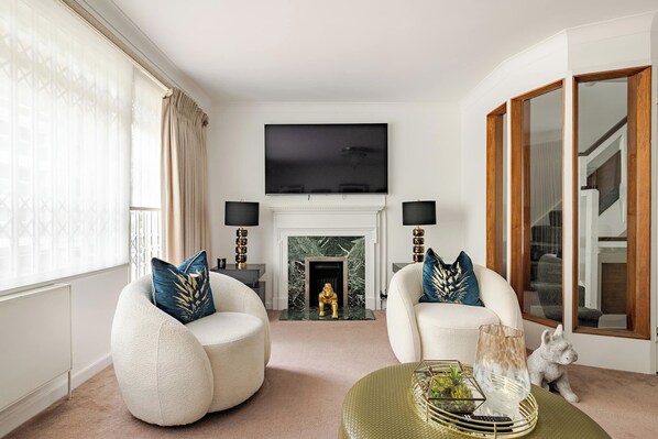 Una sala de estar con dos sillones, una chimenea, un televisor de pantalla plana y un ventanal con cortinas.