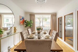 Un comedor con una mesa grande, sillas, un candelabro, un espejo y un ventanal con cortinas.