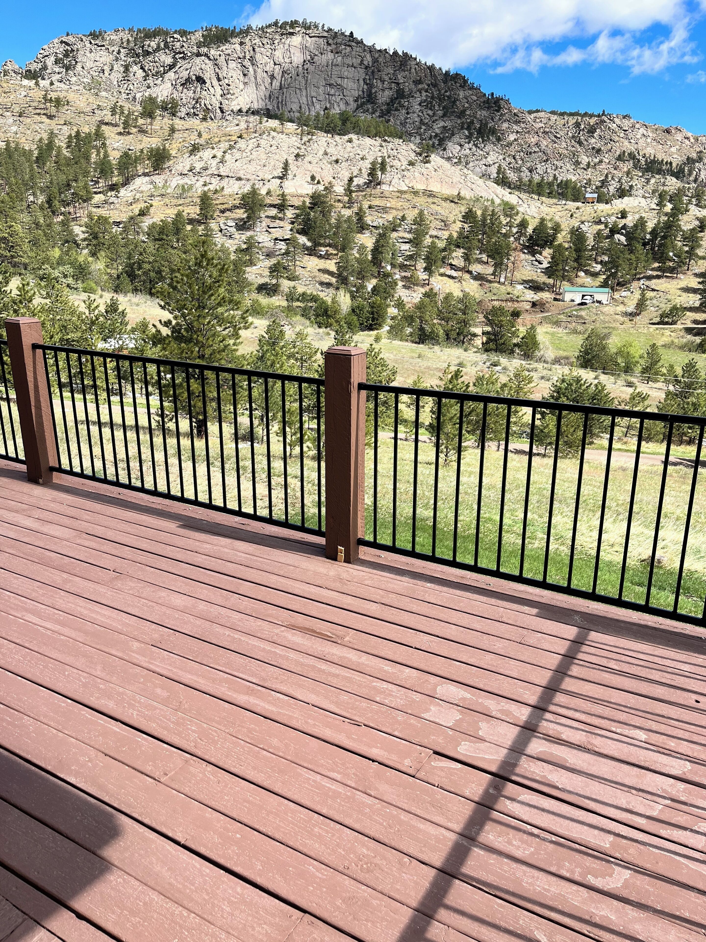 Une terrasse en bois, dotée d’une rambarde métallique, offre une vue sur un paysage montagneux à la végétation clairsemée.