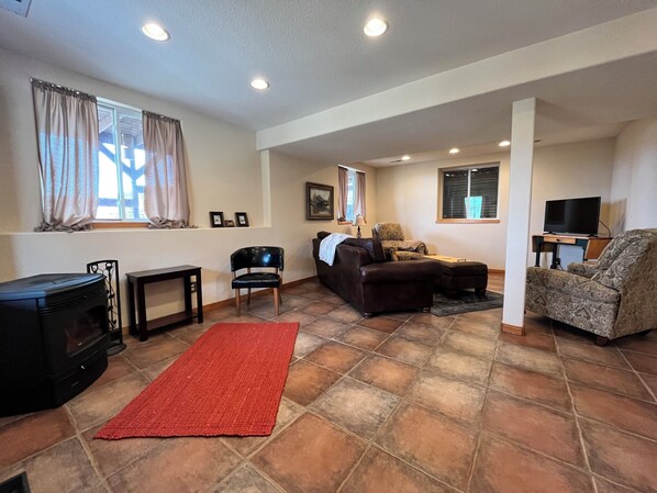 A living room with a fireplace, a sofa, a chair, and a television. - Quiet Cabin with Mountain Views (Drake)