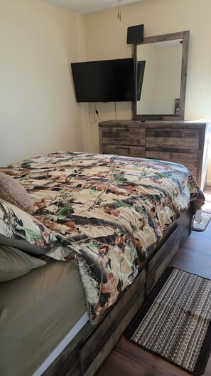 A bedroom with a bed, a dresser, a television mounted on the wall, and a mirror above the dresser.