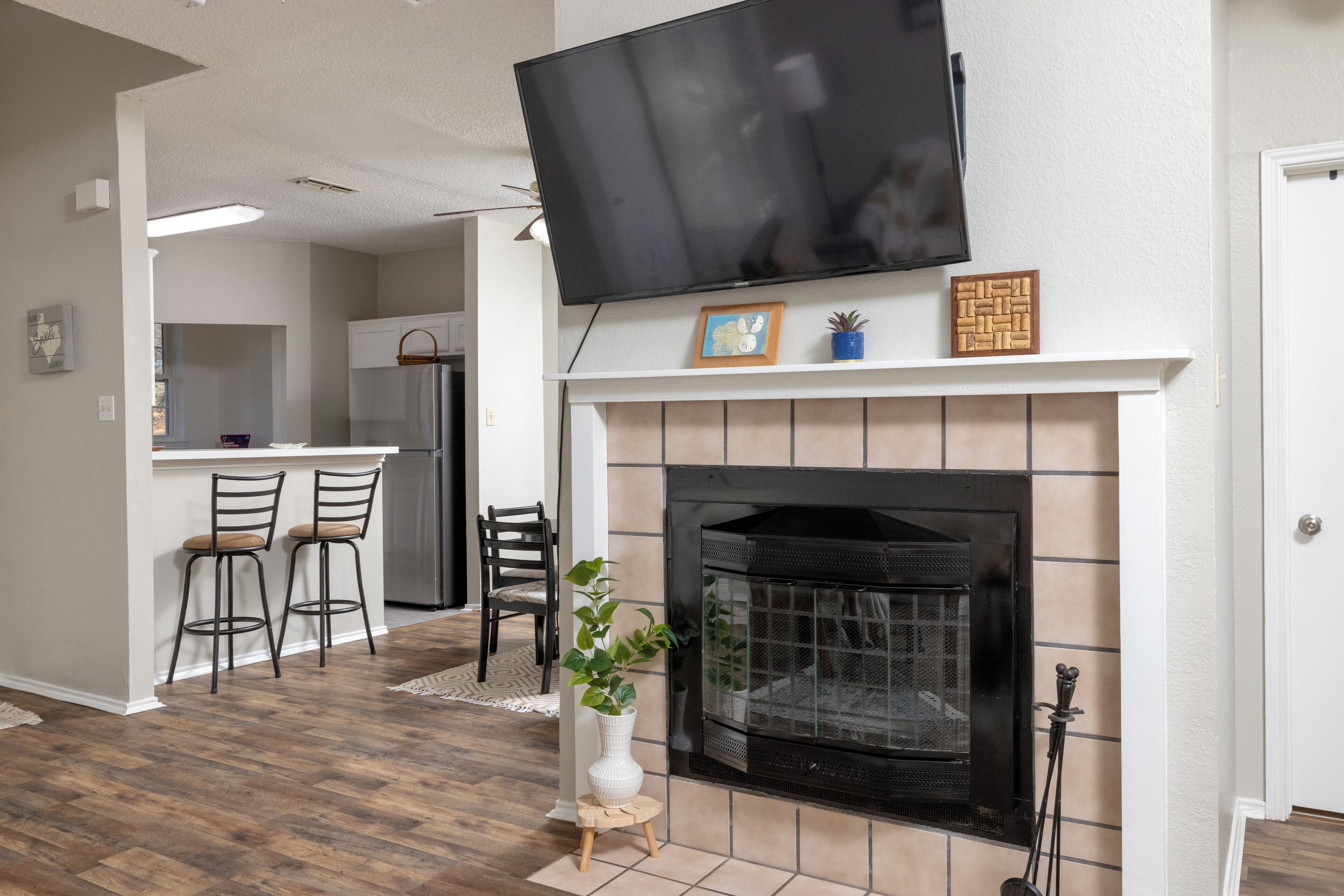 Una sala de estar con chimenea, un televisor colocado encima y una cocina al fondo.