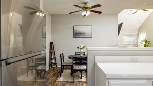 A modern kitchen with a refrigerator, a dining table with chairs, a ceiling fan, and a window with blinds. - Private Backyard + Deck - Near DFW + Toyota Music (Euless)