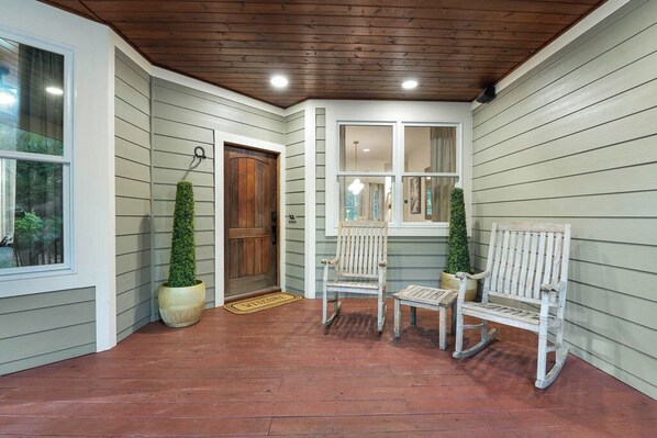 A covered porch with a wooden ceiling, a bench, a chair, and a potted plant.