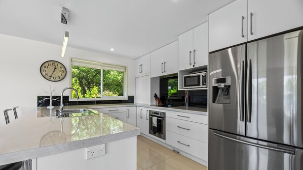 Una cocina moderna con armarios blancos, electrodomésticos de acero inoxidable, una isla grande y una ventana con vistas a zonas verdes.