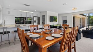 Una cocina moderna con armarios blancos, electrodomésticos de acero inoxidable y un comedor con mesa de madera dispuesta para seis personas.