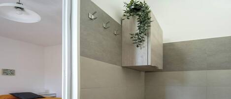 A bathroom with a toilet, a sink, and a shower area. There is a bed with an orange bedspread in the adjacent room.