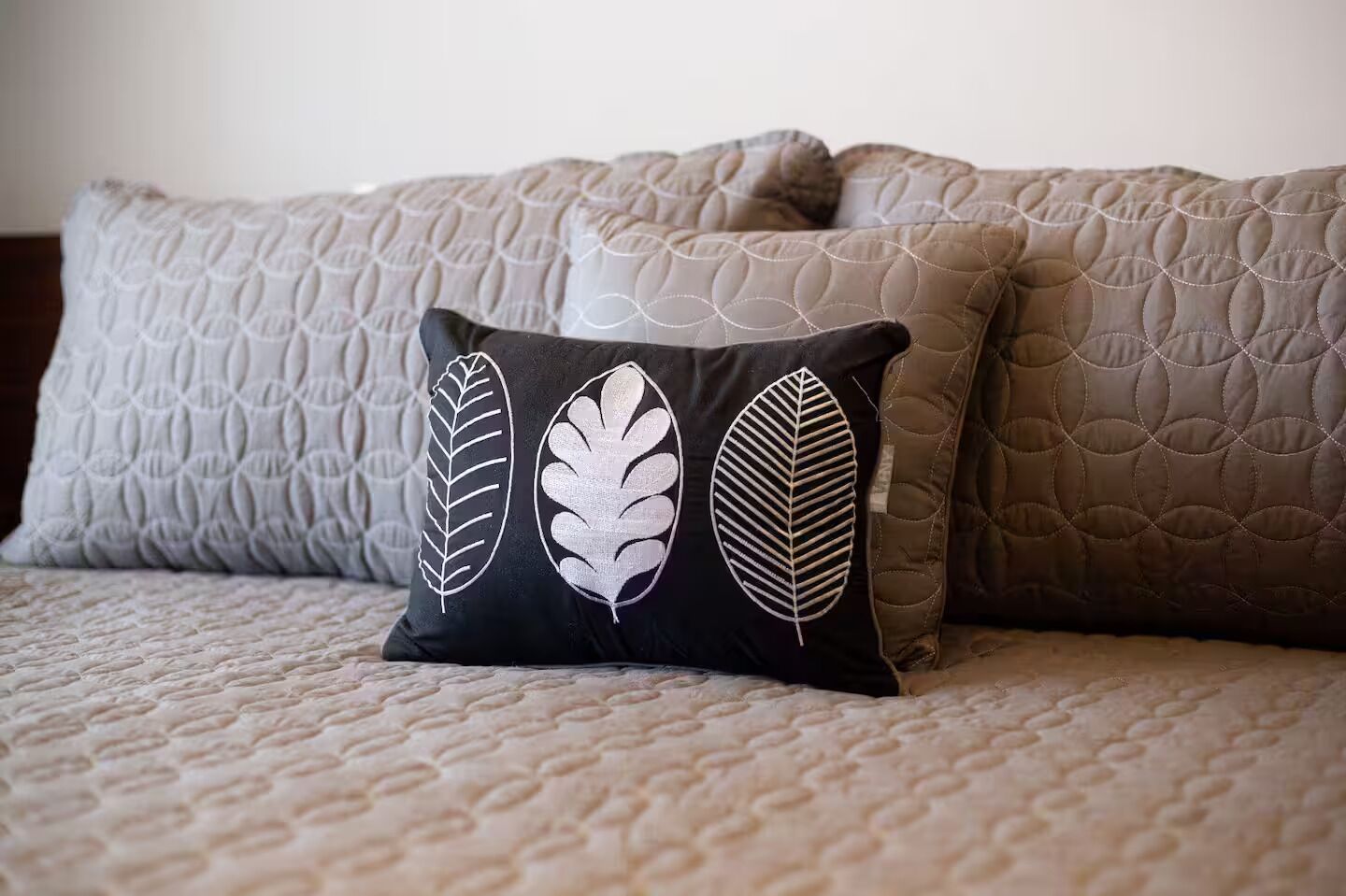 A bed with a quilted cover and three pillows, one with a leaf pattern.