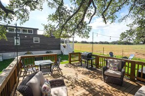 A wooden deck with outdoor furniture, a grill, and a view of a grassy field.