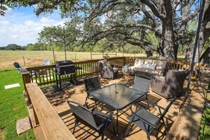 An outdoor patio with a wooden deck, a glass table, black metal chairs, wicker sofas, and a barbecue grill.