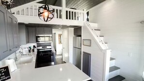 Une cuisine moderne avec un îlot central, un escalier et un panneau d’accueil.