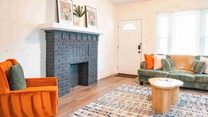 Un salon avec une cheminée en briques, un canapé vert et un tapis à motifs.