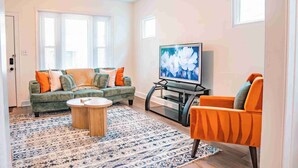 Un salon avec un canapé vert, un fauteuil orange et un téléviseur à écran plat.