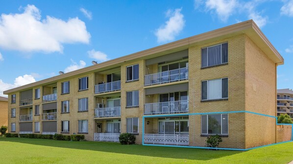 A multi-story apartment building with balconies, a flat roof, and a well-maintained lawn.