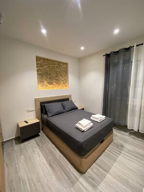 Une chambre moderne avec un grand lit, une table de chevet, une lampe fixée au mur et un rideau.