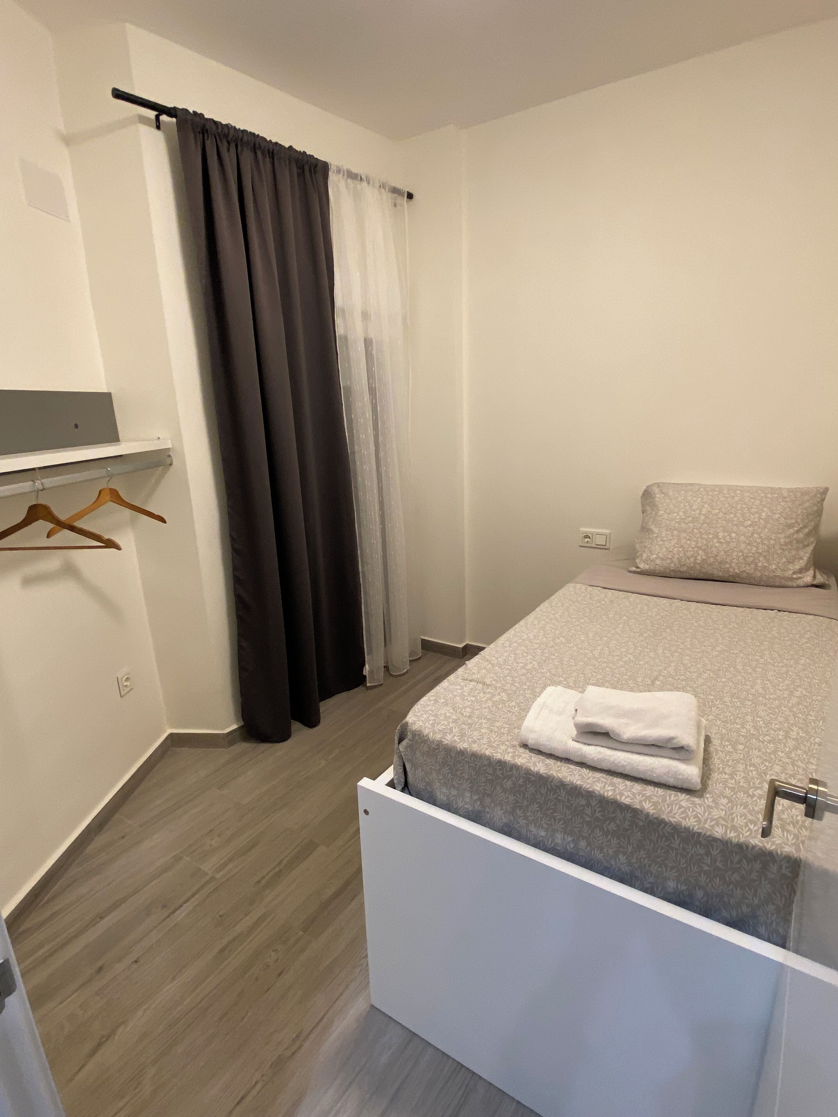 Un dormitorio con cama, mesita de noche, toalla colgada, armario y cortina de ducha.