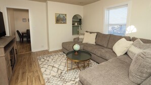 A living room with a sectional sofa, a glass coffee table with a globe, a patterned rug, and a wooden cabinet.